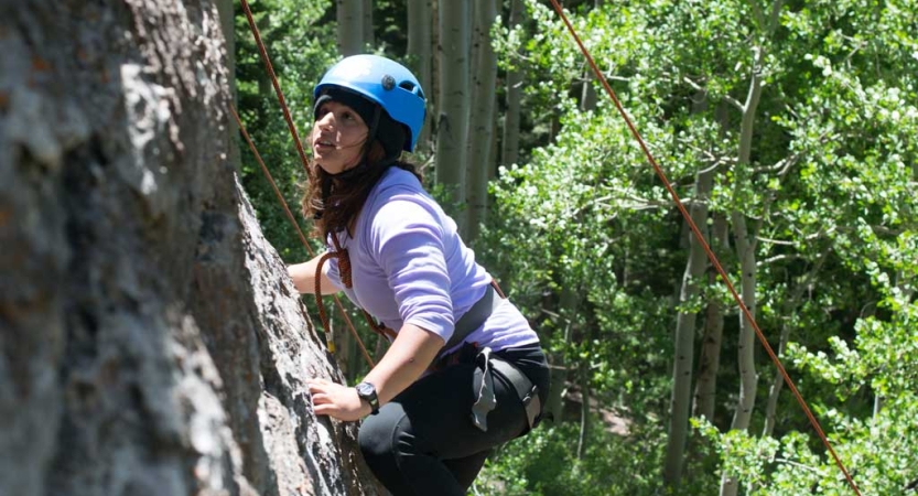 A person wearing safety gear is secured by ropes as they climb a rock wall. 